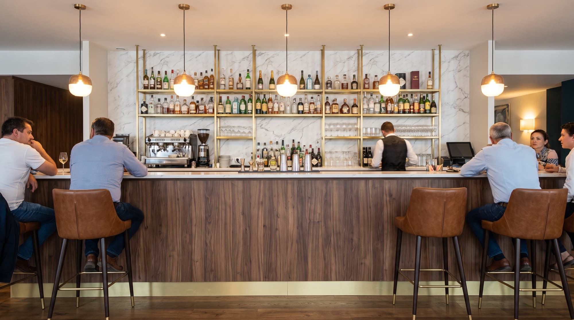 Bar d'hôtel avec comptoir en finition noyer et mur en marbre